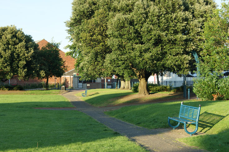 Two paths going through a park, with benches next to the paths. 